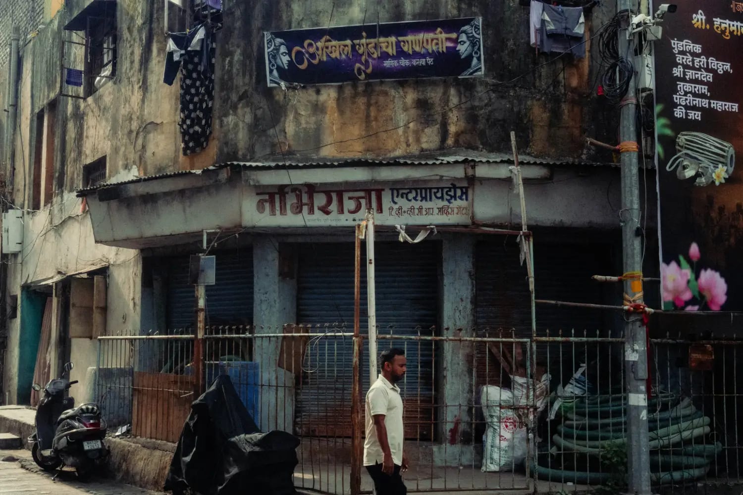 The corner of an old building with painted Marathi signboards and a shuttered shopfront below