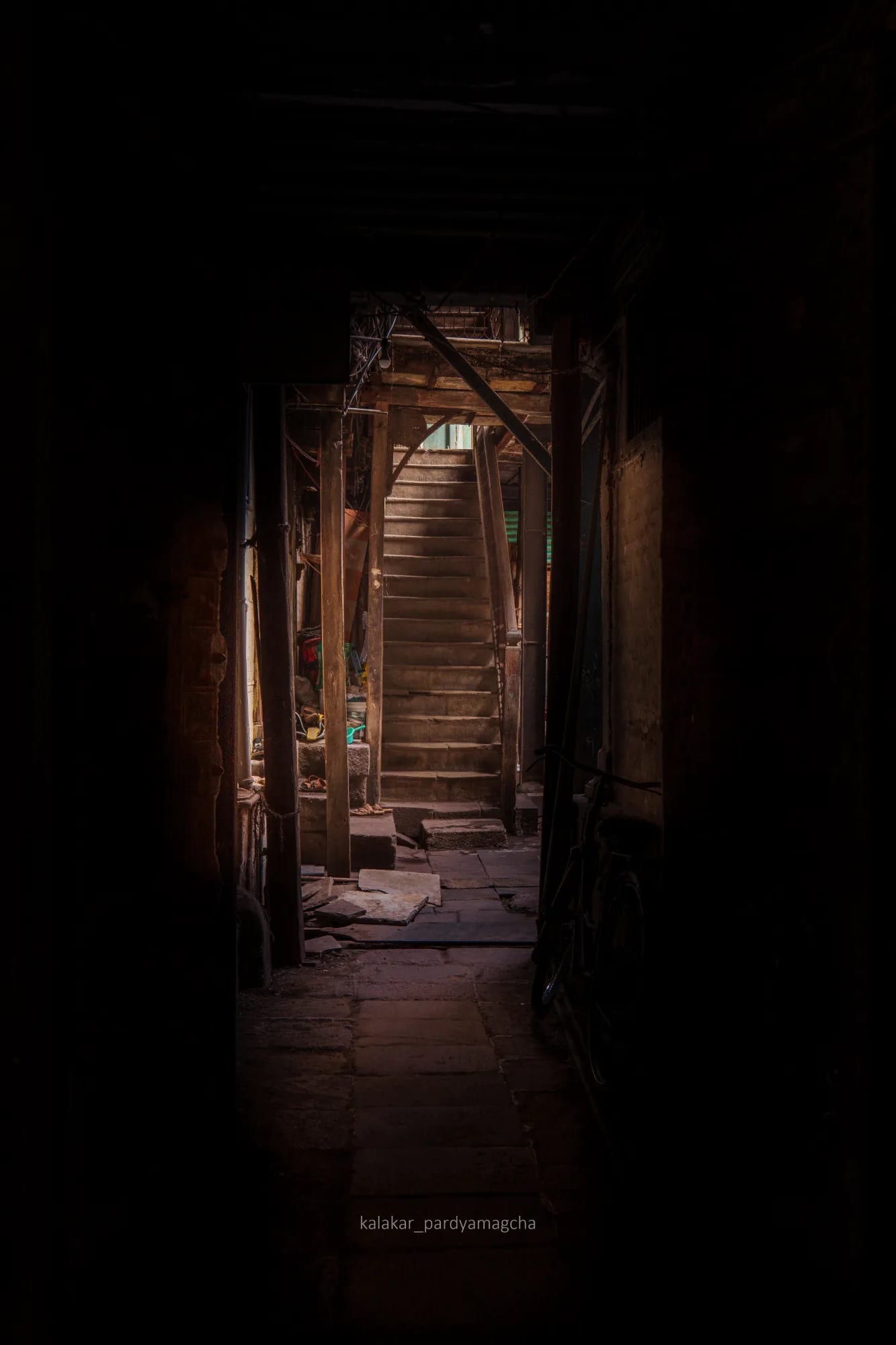 A dark corridor in an old building leading to a lit staircase at the far end