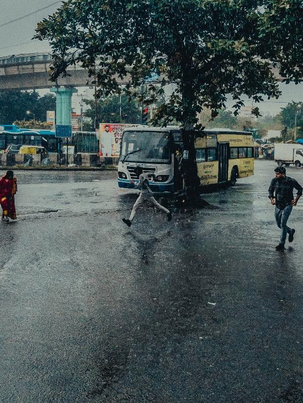 People running across a wet road in the rain, buses waiting at a stand behind them