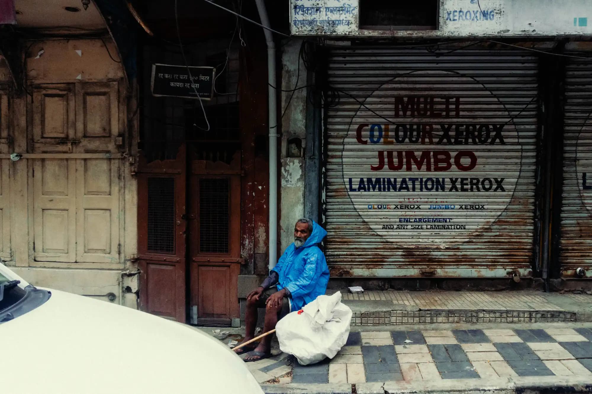 A man resting outside a shuttered shopfront beneath a painted Multi Colour Xerox sign